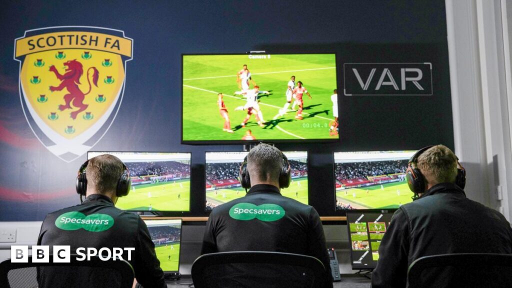Referees in a VAR room watching the monitors with their backs to the camera